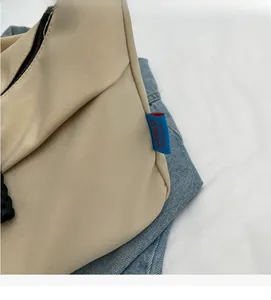 Detail of beige nylon crossbody bag showing premium stitching and blue textile label