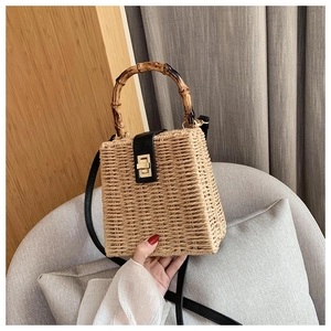Detail of straw woven box bag with bamboo handle and black leather strap and metal twist lock
