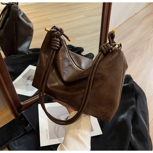 Detail of dark brown leather tote featuring knot shoulder strap and gold hardware
