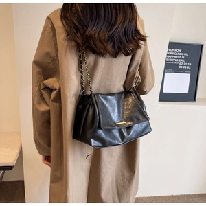 Détail d'un sac cabas noir texturé avec bandoulière chaîne dorée sur un trench