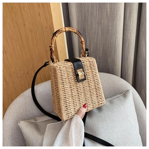 Close-up of woven straw handbag with bamboo handle, leather flap, and gold lock detail