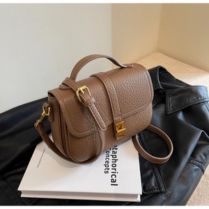 Detail of retro brown leather crossbody bag with golden clasp on an art book