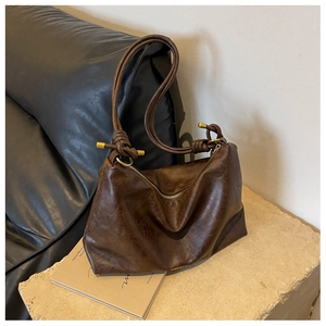 Detail of dark brown tote bag featuring knot shoulder strap and golden metal accents