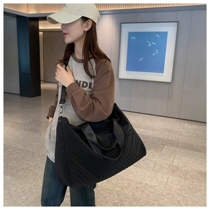 Detail of black quilted travel bag with diamond texture and detachable shoulder strap