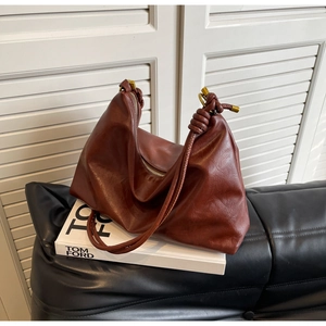 Detail of dark brown leather hobo bag featuring knotted shoulder strap and gold hardware
