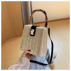 Detailed view of woven straw handbag featuring bamboo handle and golden metal twist lock