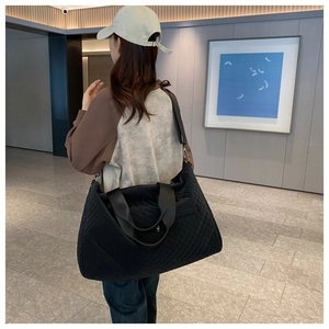 Rear view of a model carrying a large black quilted nylon travel bag with shoulder strap