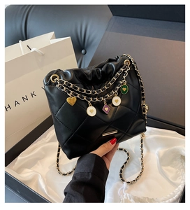 Détail d'un sac matelassé noir avec chaîne dorée et breloques en forme de cœur