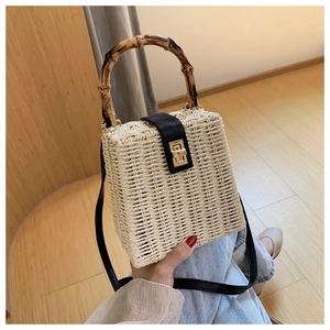Detailed shot of beige straw handbag featuring bamboo handle and leather flap with gold lock