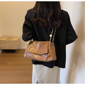 Détail d'un sac bandoulière en cuir marron avec chaîne dorée et fermoir porté par un mannequin