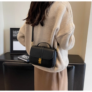 Close-up of black leather crossbody bag with gold buckle on a model's back