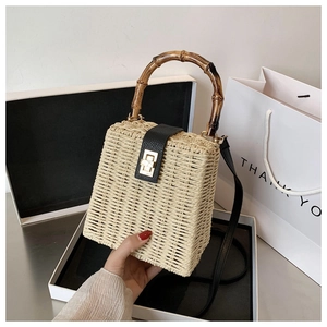 Detail of straw handbag with bamboo handle, leather strap and golden turn-lock closure