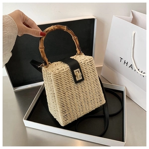 Detail of woven straw bag with carbonized bamboo handle and black leather strap