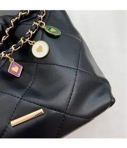 Détail d'un sac seau en cuir noir matelassé avec chaîne dorée et breloques de cœur