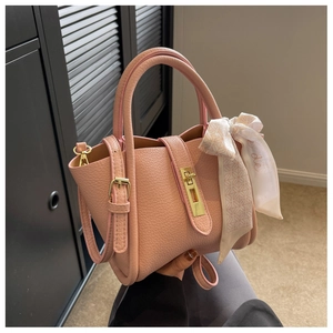 Detail of pink lychee leather handbag featuring gold clasp and decorative silk scarf