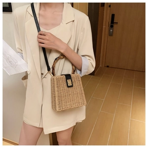 Detail of woven straw bag with bamboo handle, black leather flap and gold twist lock