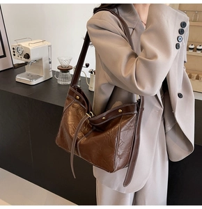 Close-up of brown textured leather tote bag featuring contrast white stitching and gold hardware
