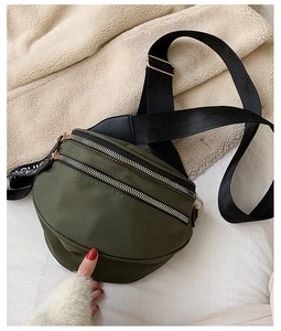 Detail view of a dark green nylon crossbody bag featuring dual golden metal zippers