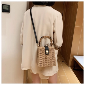 Detail of straw woven square bag featuring bamboo handles and leather twist lock strap