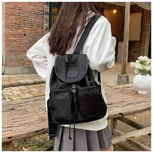 Detail of black nylon backpack featuring leather buckle straps and drawstrings