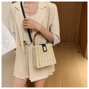 Detail of hand-woven straw bag featuring a bamboo handle and gold metal twist lock buckle