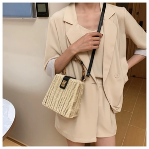 Handwoven straw crossbody bag with bamboo handle worn with a beige suit in a studio