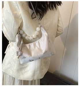 Detail of cream jacquard satin bag with pearl strap and floral pattern on a shoulder