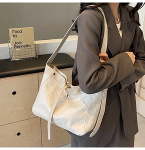 Detail of white pleated tote bag with metal rivet accents and slim shoulder strap