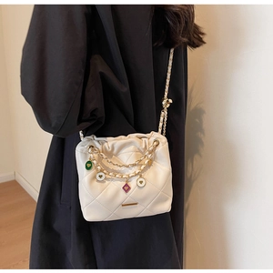 Détail du sac seau matelassé blanc avec breloques en émail coloré et bandoulière dorée