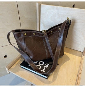 Detail of dark brown tote bag with contrast stitching and metal studs on a wooden shelf