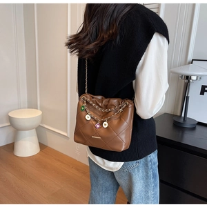 Détail du sac seau marron matelassé avec chaînes dorées et breloques cœurs