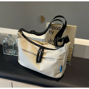 Detail view of beige nylon crossbody bag with black zippers and woven shoulder strap