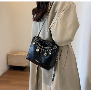 Détail du sac matelassé noir avec breloques cœur colorées sur un trench-coat beige