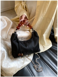 Detail of black pleated shoulder bag with amber beaded handle and floral pattern