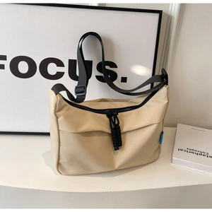 Detail shot of a beige nylon crescent bag with black wide strap on a minimalist desk