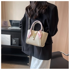 Detail view of cream pebble leather bucket bag with silk scarf on handle and gold lock
