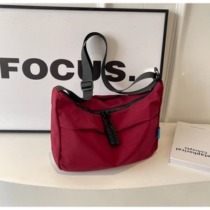 Detail of burgundy nylon dumpling bag showing black strap and woven zipper puller