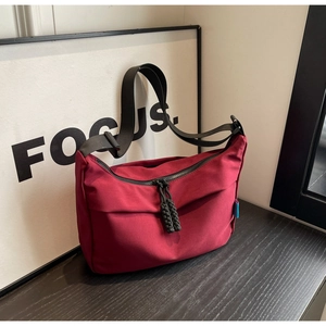 Macro detail of wine red nylon crossbody bag with black braided rope zipper and woven strap