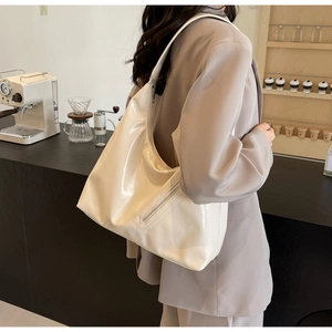 Beige faux leather crescent tote bag worn by a model in a cozy cafe setting