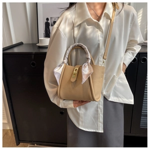 Detail of khaki pebbled leather bucket bag with silk scarf on handle and gold twist lock