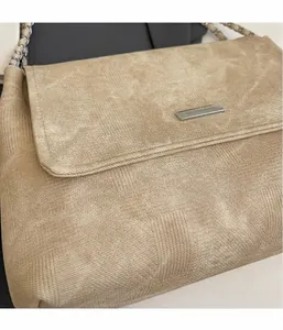 Detail der beigen Schultertasche mit Silberkette und rechteckigem Metall-Logo-Emblem
