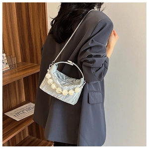 Detail van zilveren crossbodytas met parelhandvat en metalen geplooide textuur