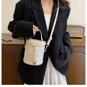 Lace embroidery detail on a beige leather cylinder bucket bag with gold hardware