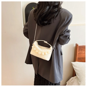 Detail van de crème crossbodytas met parelhandvat en zilveren ketting op het model