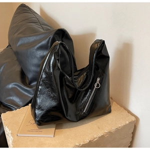 Detail of glossy black leather hobo bag with metal zipper and round puller on stone