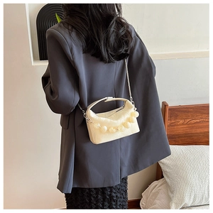 Detail van crèmewitte leren crossbodytas met decoratieve kraal en kettingriem