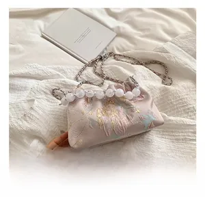 Détails de broderie sur sac en soie rose avec poignée en perles et chaîne métal