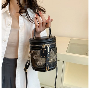 Close-up of golden butterfly embroidery on black leather cylinder bucket bag with dual zippers