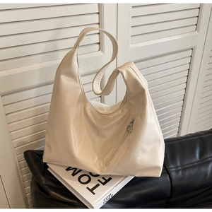 Detail of an ivory leather hobo bag with a functional diagonal zipper on a black sofa
