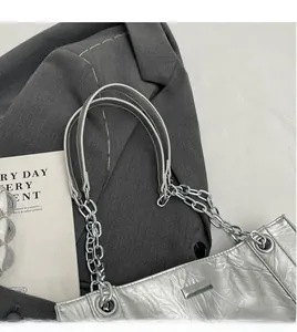 Makro-Detail der silbernen Faltenhandtasche mit Metall-Logo und Leder-Kettengurt
